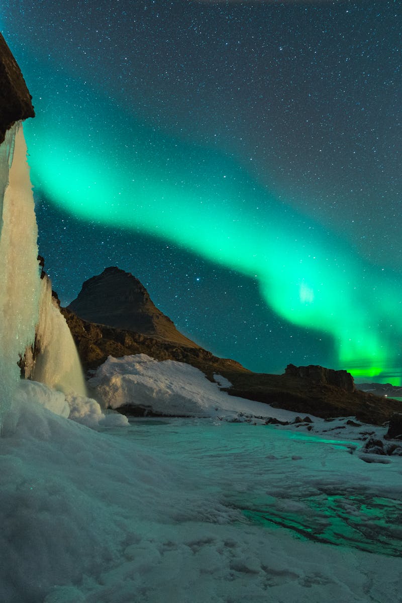 Stunning view of the Northern Lights over Kirkjufell mountain and frozen waterfall in Iceland. Perfect for nature lovers.